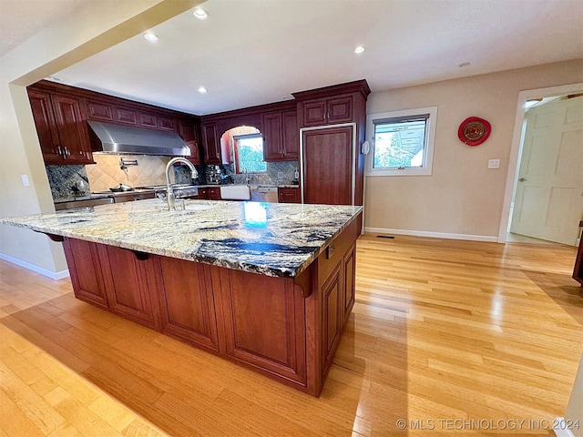 kitchen with a center island with sink, decorative backsplash, light stone countertops, and light hardwood / wood-style floors