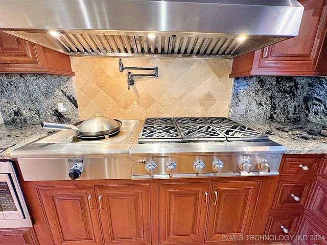 kitchen with wall chimney range hood, stainless steel gas stovetop, tasteful backsplash, and light stone counters