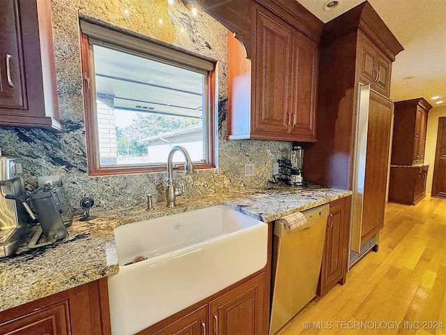 kitchen featuring light stone countertops, sink, dishwasher, light wood-type flooring, and backsplash