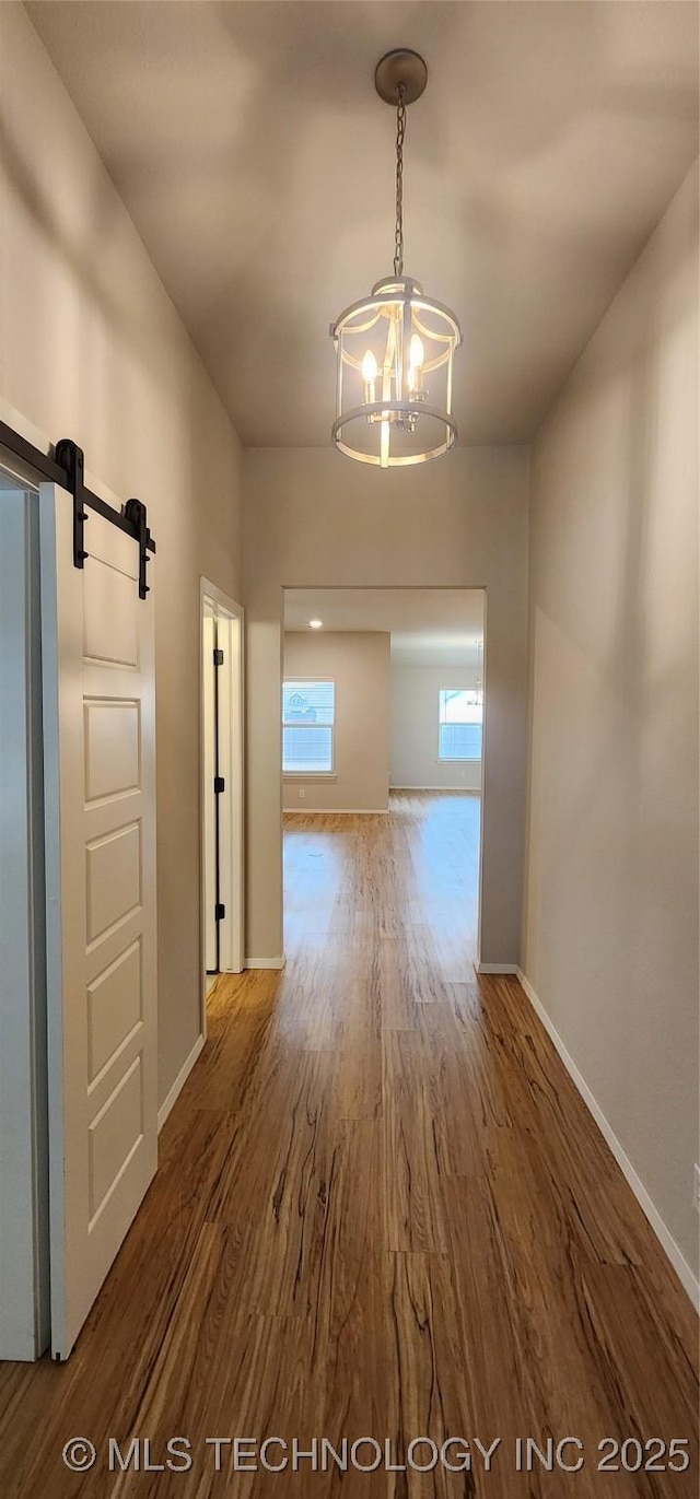 hallway with a barn door, an inviting chandelier, and hardwood / wood-style flooring