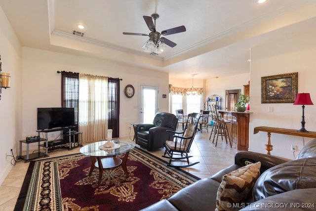 tiled living room with ornamental molding, a tray ceiling, and ceiling fan with notable chandelier