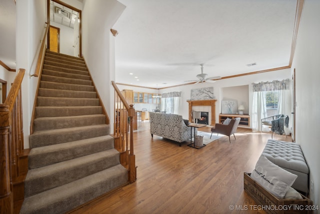 living room with ceiling fan, wood-type flooring, ornamental molding, and a tile fireplace