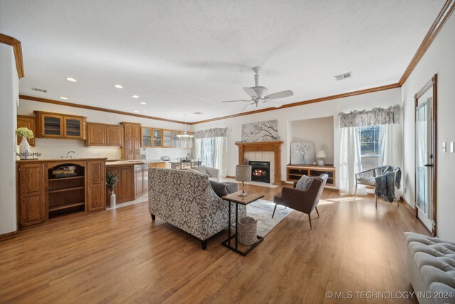 living room featuring ceiling fan, radiator, light wood-type flooring, ornamental molding, and a tile fireplace