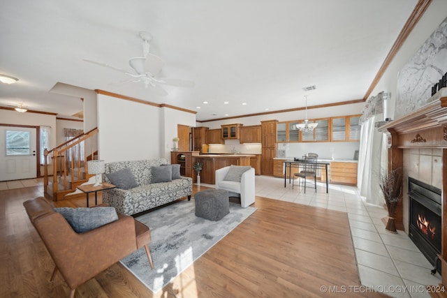 living room featuring crown molding, a tiled fireplace, ceiling fan, and light tile patterned floors