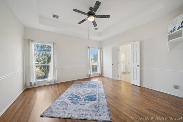 bedroom with ceiling fan, a raised ceiling, multiple windows, and hardwood / wood-style floors