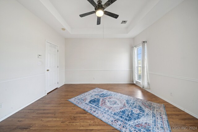 unfurnished room with ceiling fan, dark wood-type flooring, and a raised ceiling