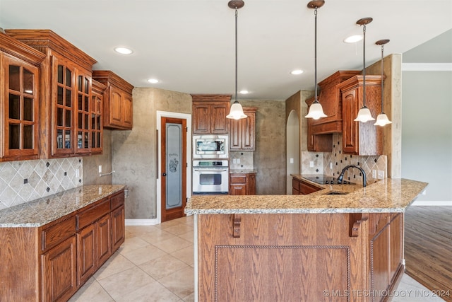 kitchen featuring decorative backsplash, kitchen peninsula, stainless steel appliances, sink, and pendant lighting