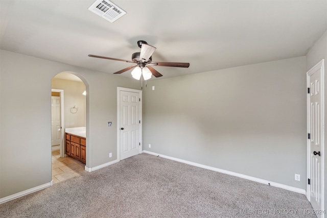 unfurnished bedroom with light carpet, ensuite bathroom, and ceiling fan