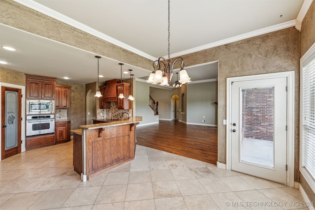 kitchen with kitchen peninsula, hanging light fixtures, appliances with stainless steel finishes, ornamental molding, and light hardwood / wood-style floors