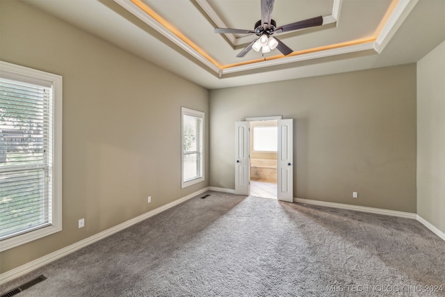 carpeted empty room featuring ceiling fan, a tray ceiling, and plenty of natural light