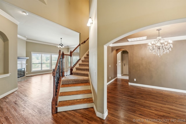 staircase featuring crown molding, hardwood / wood-style flooring, a high ceiling, and ceiling fan with notable chandelier