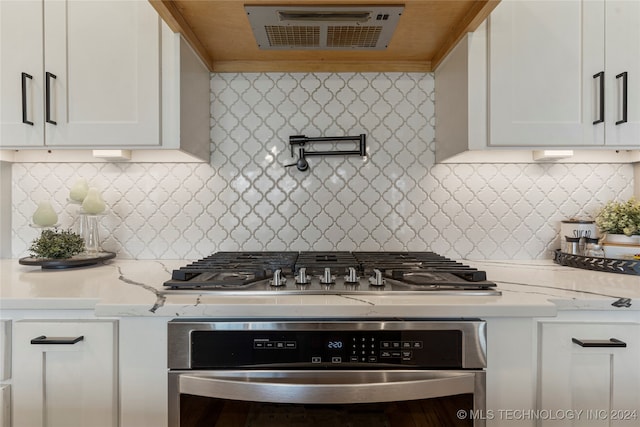 kitchen featuring range hood, appliances with stainless steel finishes, white cabinets, and backsplash