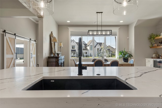 kitchen featuring light stone countertops, a barn door, decorative light fixtures, and beverage cooler