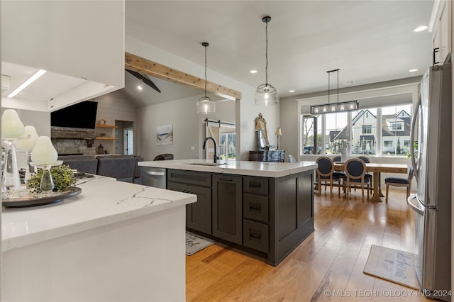 kitchen featuring sink, lofted ceiling with beams, a stone fireplace, stainless steel appliances, and light hardwood / wood-style flooring