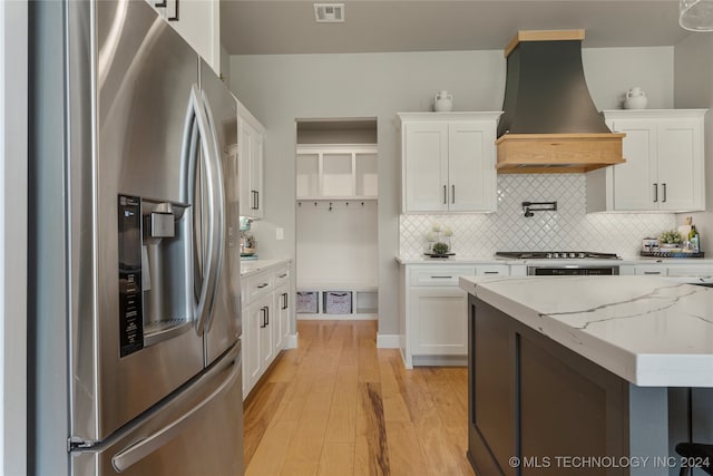 kitchen with custom exhaust hood, white cabinets, light hardwood / wood-style flooring, and stainless steel appliances