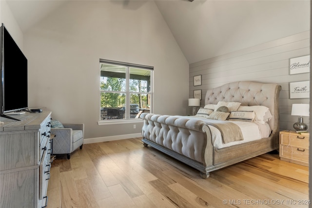 bedroom featuring light hardwood / wood-style floors, wood walls, and high vaulted ceiling