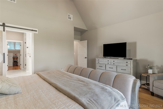 bedroom featuring a barn door, high vaulted ceiling, and light wood-type flooring