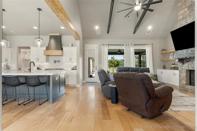 living room featuring light wood-type flooring, a stone fireplace, ceiling fan, beamed ceiling, and high vaulted ceiling