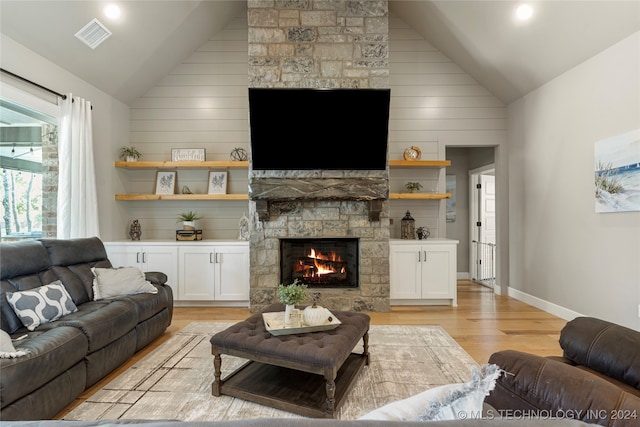 living room featuring a stone fireplace, high vaulted ceiling, light hardwood / wood-style floors, and wood walls