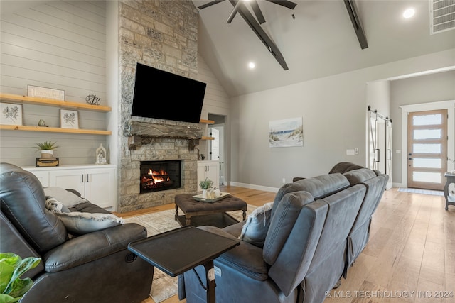 living room featuring a barn door, a fireplace, ceiling fan, high vaulted ceiling, and light hardwood / wood-style flooring