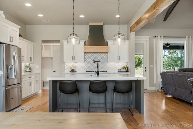 kitchen featuring premium range hood, stainless steel fridge with ice dispenser, hanging light fixtures, and white cabinets