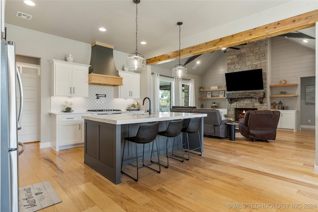 kitchen featuring vaulted ceiling with beams, white cabinets, custom exhaust hood, appliances with stainless steel finishes, and light hardwood / wood-style floors