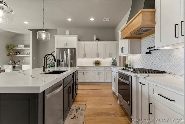 kitchen featuring stainless steel appliances, sink, decorative light fixtures, white cabinetry, and premium range hood