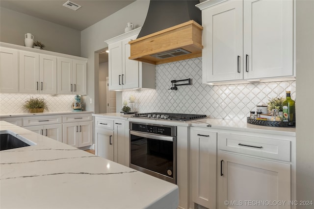 kitchen featuring white cabinetry, custom range hood, stainless steel appliances, and tasteful backsplash