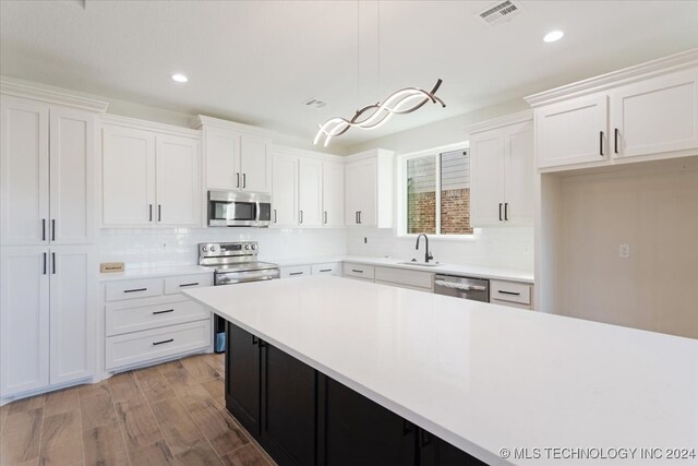 kitchen featuring sink, pendant lighting, light wood-type flooring, white cabinetry, and appliances with stainless steel finishes