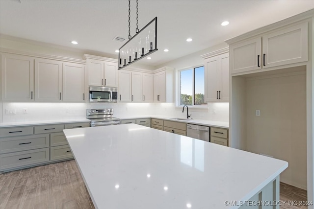 kitchen with a kitchen island, appliances with stainless steel finishes, decorative light fixtures, and light hardwood / wood-style floors