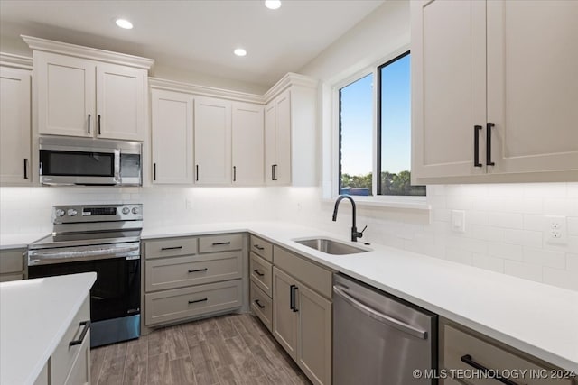 kitchen with stainless steel appliances, backsplash, sink, hardwood / wood-style floors, and white cabinetry