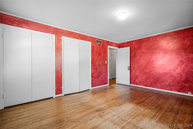 unfurnished bedroom with multiple closets, hardwood / wood-style floors, and ornamental molding