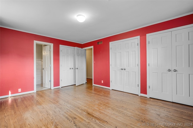 unfurnished bedroom featuring light hardwood / wood-style flooring, ornamental molding, two closets, and connected bathroom