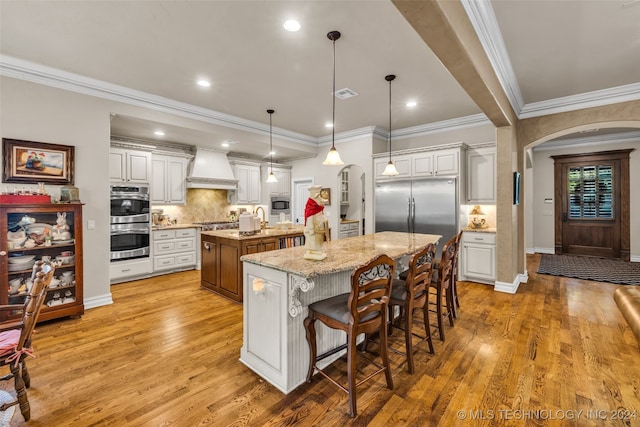 kitchen with white cabinets, a center island with sink, light wood-type flooring, pendant lighting, and stainless steel appliances