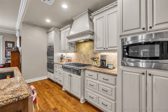 kitchen with light hardwood / wood-style flooring, ornamental molding, appliances with stainless steel finishes, white cabinetry, and premium range hood