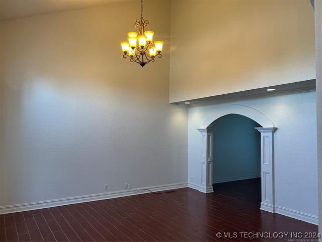 unfurnished room featuring a towering ceiling, an inviting chandelier, and dark wood-type flooring