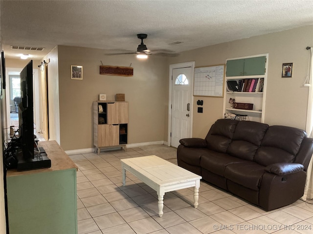 living area featuring light tile patterned floors, visible vents, a ceiling fan, a textured ceiling, and baseboards