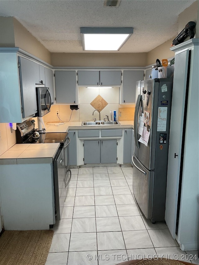 kitchen featuring appliances with stainless steel finishes, gray cabinets, a textured ceiling, light countertops, and a sink