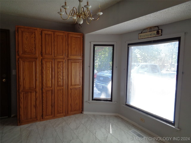 unfurnished dining area featuring a wealth of natural light, a notable chandelier, and a textured ceiling