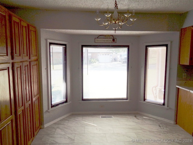 unfurnished dining area featuring a notable chandelier, a textured ceiling, and plenty of natural light