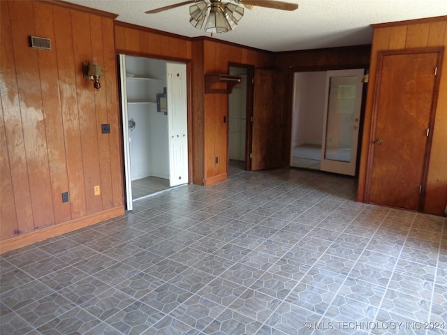 empty room with a textured ceiling, wooden walls, and ceiling fan