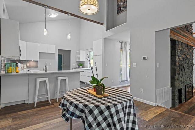 dining space with high vaulted ceiling, dark hardwood / wood-style floors, a stone fireplace, and sink