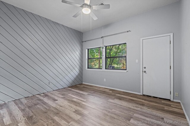 spare room with wood-type flooring, ceiling fan, and wooden walls