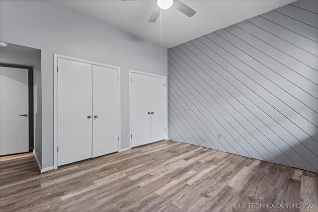 unfurnished bedroom featuring ceiling fan, light hardwood / wood-style flooring, and wood walls