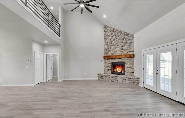 unfurnished living room with a stone fireplace, light hardwood / wood-style flooring, high vaulted ceiling, and french doors