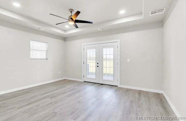 spare room with a raised ceiling, ceiling fan, light wood-type flooring, and french doors