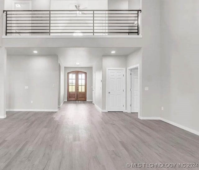 foyer with a towering ceiling, french doors, and light wood-type flooring