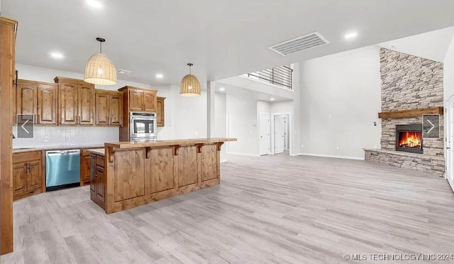 kitchen with hanging light fixtures, light wood-type flooring, a kitchen island, stainless steel appliances, and a fireplace