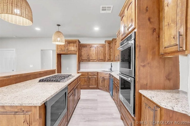 kitchen with sink, stainless steel appliances, light stone counters, light hardwood / wood-style flooring, and pendant lighting