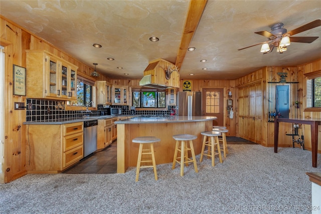 kitchen with stainless steel appliances, ceiling fan, dark colored carpet, a kitchen island, and wood walls